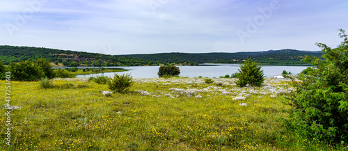 panoramic of green field with wild flowers and azure blue lake. Spain.