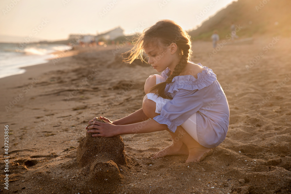 Portrait of beautiful little girl builds a sand castle in sunset light ...