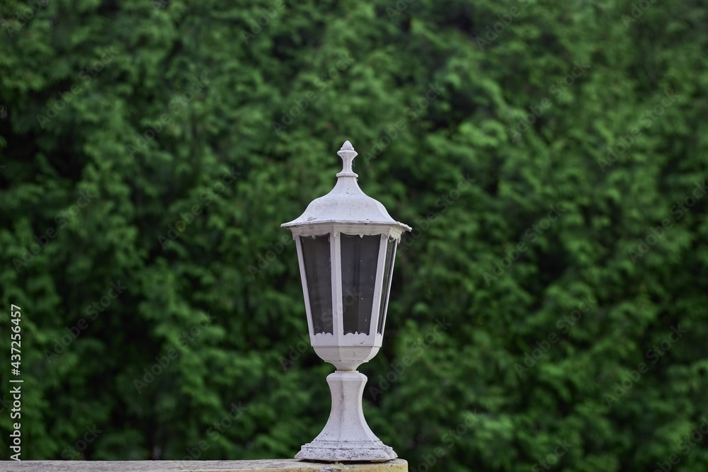 Street white lamp. Green natural background. An old fashioned street lamp. Background blurred, focus only on the lamp.
