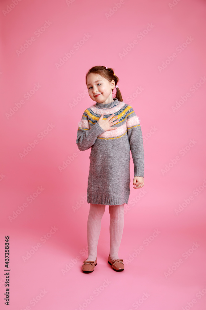 Portrait of little funny smiling girl showing to themself in warm dress on rosa background Portrait of little funny smiling girl showing to themself in warm dress on rosa background