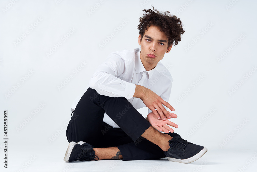 young man with curly hair sits cross-legged on the floor young man with curly hair sits cross-legged on the floor