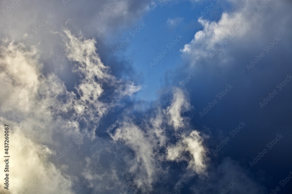 Fototapeta premium White thunderclouds in the clear blue sky. Heavenly landscape after a thunderstorm. Bright colorful thunder clouds in the sun light. Picturesque clouds in the evening light. Abstract bright skyscape.