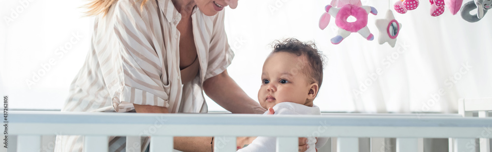 woman smiling near infant african american child in crib, banner woman smiling near infant african american child in crib, banner