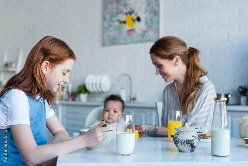 preteen girl having breakfast near mother and infant african american sister