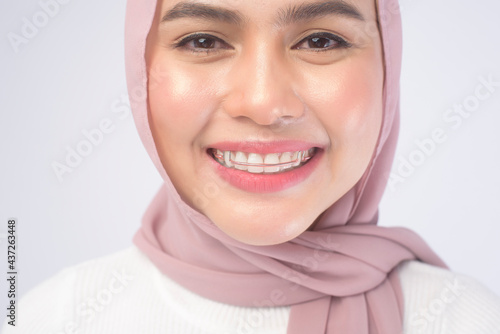 Young muslim woman holding colorful retainer for teeth over white background studio, dental healthcare and Orthodontic concept.