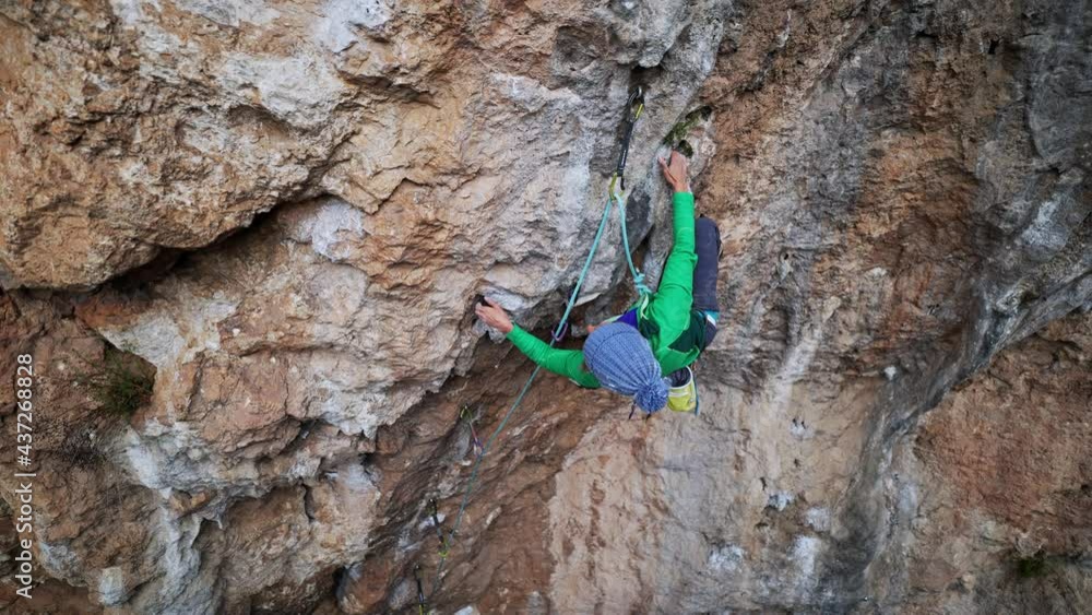 slow motion aerial view strong moman rock climber climbs on overhanging crag by hard challenging route. woman makes tough effort and reaches holds for leg slow motion aerial view strong moman rock climber climbs on overhanging crag by hard challenging route. woman makes tough effort and reaches holds for leg