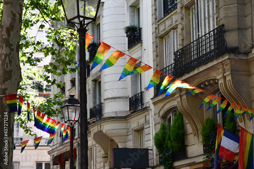 Decoration of triangle shape banners in colors of Lgbtq flags hanging between vintage lantern streetlights and ornate house with balconies. Gay pride parade symbols and French flag in Paris, France