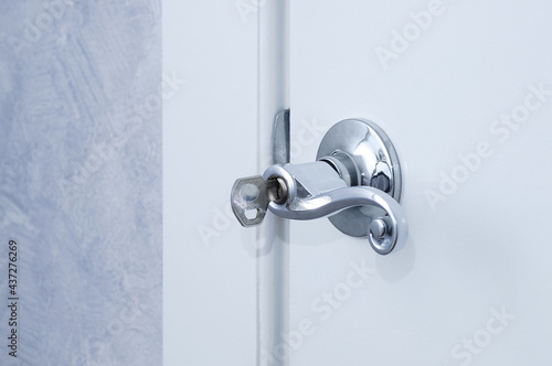 Metallic gray handle with key on a white closed door in a room.