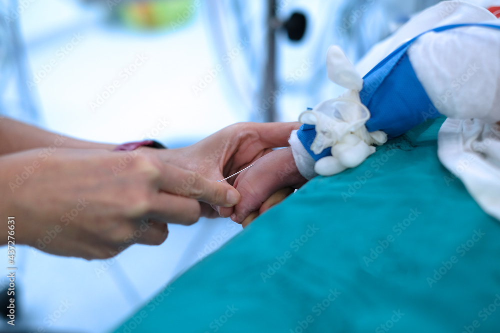 Doctor holding baby’s foot and injecting with needle to baby’s foot for drawing blood sample in cardiac operating room