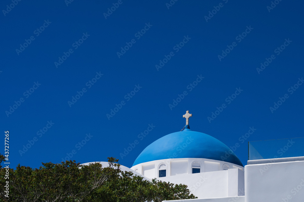 White traditional Greek Orthodox church with blue dome on the island of Santorini. Blue sky on background.