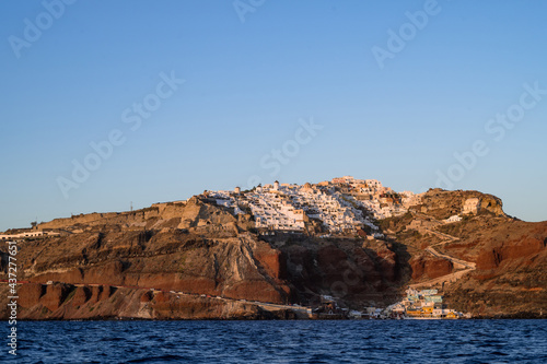 View from sea of Oia up the hill and sea port. Santorini, Greece. White city architecture. Luxury tourism. Sunset light.