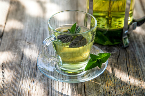 A cup with fresh scented mint tea on a wooden table in the summer garden.