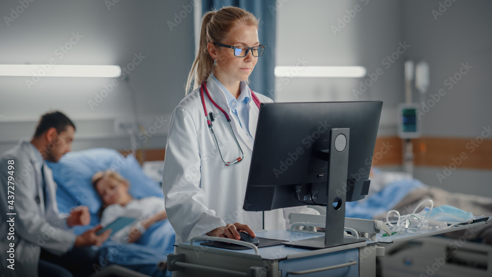 Hospital Ward: Professional Female Doctor or Surgeon Uses Medical Computer. In the Background ModernEquipment Clinic Doctor Sitting and Caring for Patient Recovering After Successful Surgery in Bed