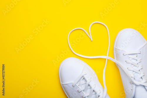 Pair of casual shoes with heart shaped laces on yellow background. Top view of stylish sneakers on color background with place for text