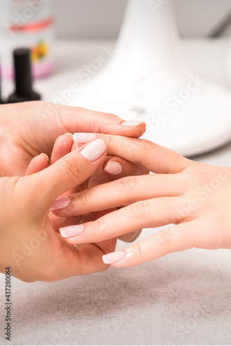 Manicure master massaging client s female fingers after nail polishing in a nail salon