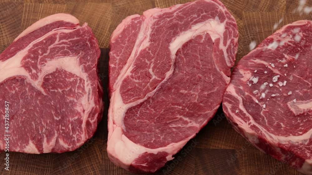 Seasoning raw ribeye beef steaks with salt Seasoning raw ribeye beef steaks with salt