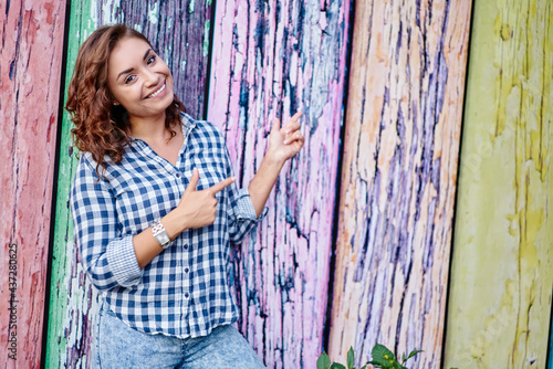 Half length portrait of cheerful hipster girl dressed in casual clothes pointing at copy space for fashion advertising, happy female model showing promotional background at publicity area in city