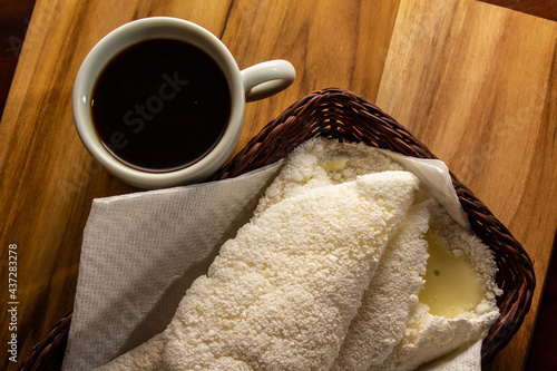 Duas tapiocas dentro de uma pequena cesta de vime e uma xícara de café sobre mesa de madeira. photo