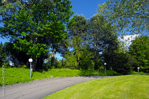 Geteerter Weg durch Park mit Kugelleuchten und Bäume und grüne Wiese und blauer Himmel bei Sonnenschein - Stockfoto photo