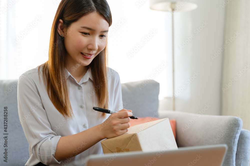 Asian woman is packing the cardboard boxes delivers to customers working from home. Female started up a small business as an online shopping Asian woman is packing the cardboard boxes delivers to customers working from home. Female started up a small business as an online shopping
