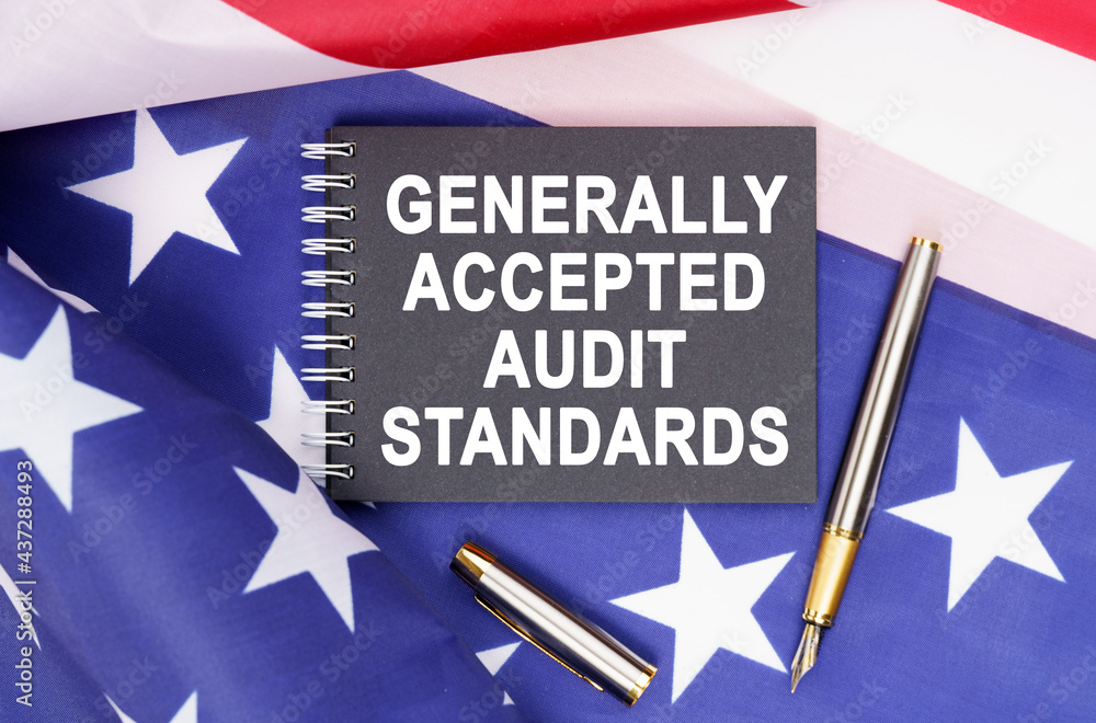 On the table is an American flag, a pen and a notebook with the inscription - GENERALLY ACCEPTED AUDIT STANDARDS On the table is an American flag, a pen and a notebook with the inscription - GENERALLY ACCEPTED AUDIT STANDARDS