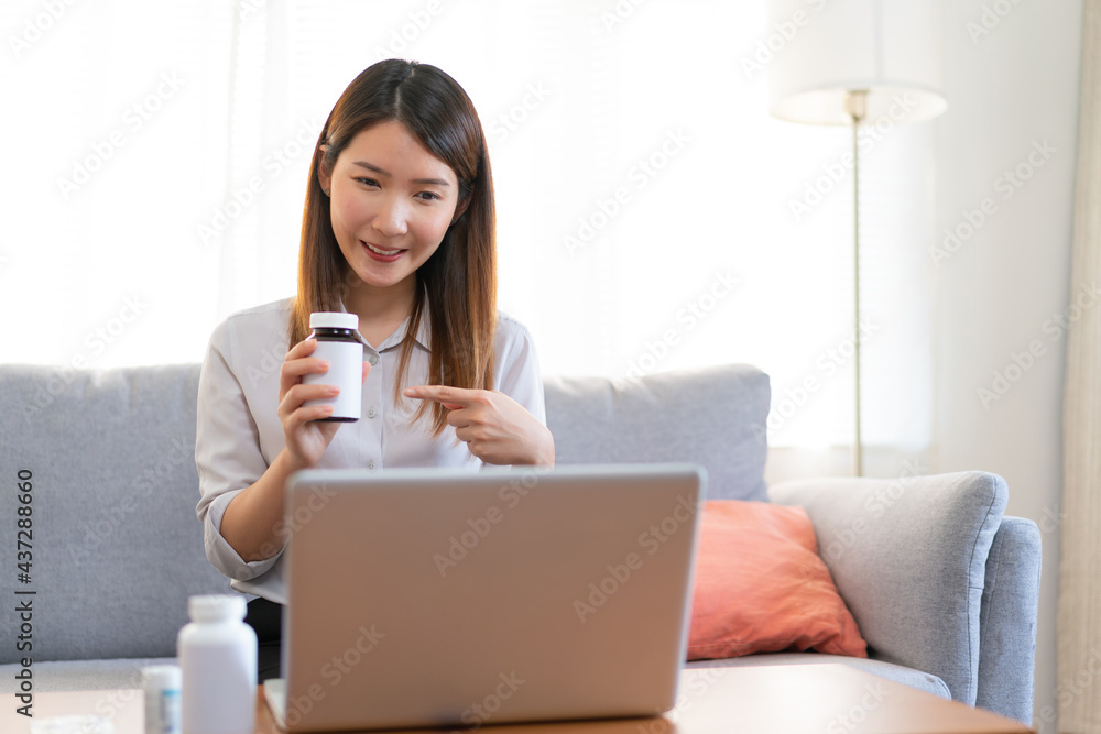 Asian female medical assistant making video call with patients for online support, Woman explaining medicine bottles working from home while coronavirus pandemic Asian female medical assistant making video call with patients for online support, Woman explaining medicine bottles working from home while coronavirus pandemic