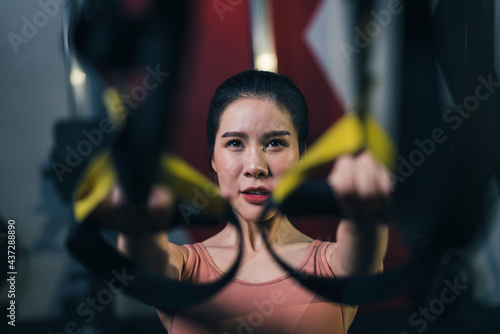 Asian female sportsperson exercising trx strap in fitness gym. Concept of bodybuilding and fitness.