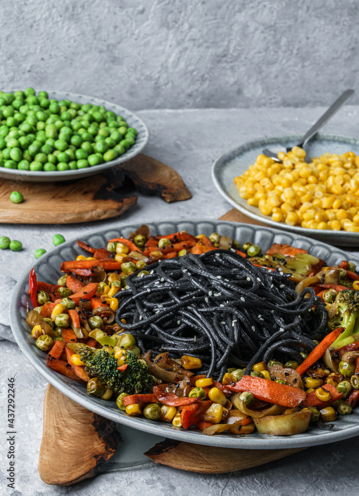 Black spaghetti or pasta from seafood with grilled vegetables, broccoli, corn, green peas in plate on light gray backgroud. Wholemeal pasta, healthy vegan food, close up