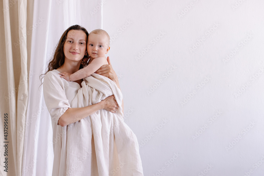 Mom hugs baby on a white background. Eco parenting concept. White clothes and a diaper  natural fabrics linen cotton muslin.  Mother's love. Hugs, smiles, happiness. Mother and child togetherness