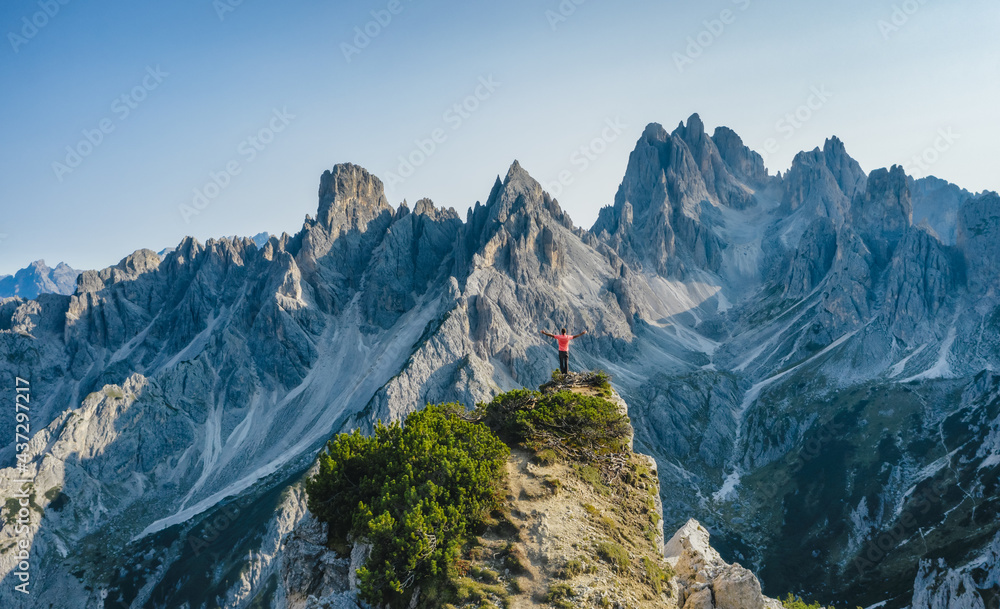 Aerial view of a man with raised hands on the top edge admiring epic Cadini di Misurina mountain peaks, Italian Alps, Dolomites, Italy, Europe
