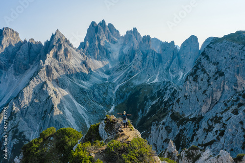 Aerial view of a women hiker with raised hands on the top edge admiring epic Cadini di Misurina mountain peaks, Italian Alps, Dolomites, Italy, Europe