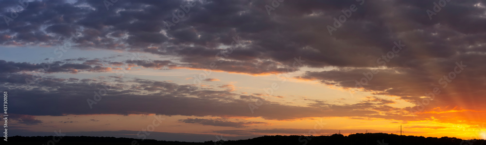 Panorama of a beautiful sunset with purple clouds and sunbeams to the horizon.