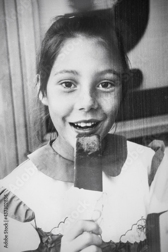 Retro portrait of a Soviet girl with ice cream popsicle. Vintage black and white paper photo. Early 1990s. Old surface, soft focus. Transferred property, family archive.