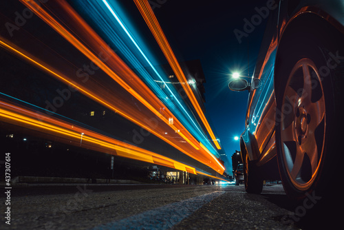 light trails at sunset with reflections on car body. low angle view from the street.
