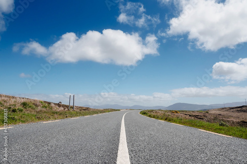 Narrow asphalt road on a warm sunny day, beautiful cloudy sky, nobody. Achill island, county Mayo, Ireland. Travel concept © mark_gusev