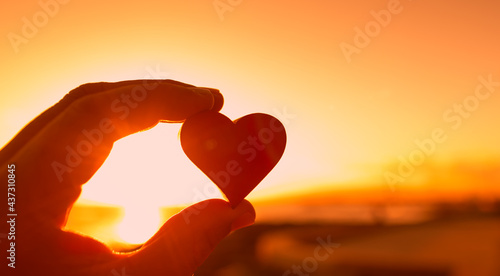 Hand holding red heart on sunset sky. 