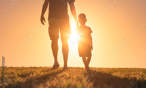 Father son holding hands walking together outdoors at sunset . Fatherhood and family togetherness concept. 