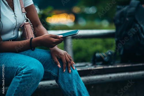 Cheerful african american woman using smartphone while sitting on a bench