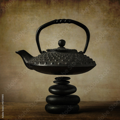 Flying teapot levitating over a pile of black massage stones on a wooden table 