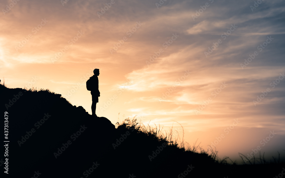 A woman standing at the top of the mountain and watching sunset