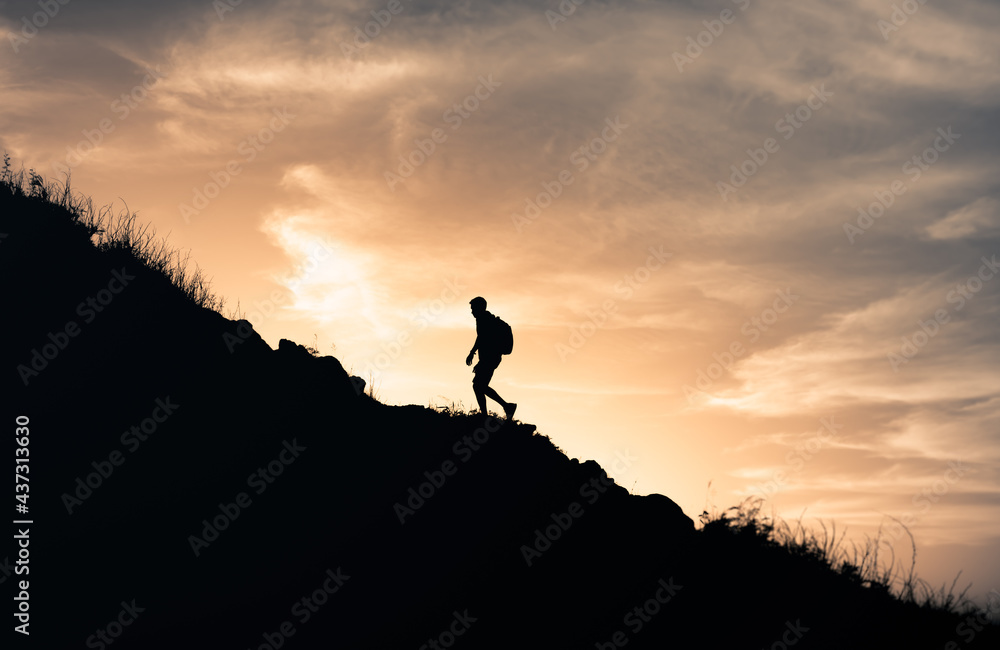 Male hiker silhouette climbing up a mountain edge.