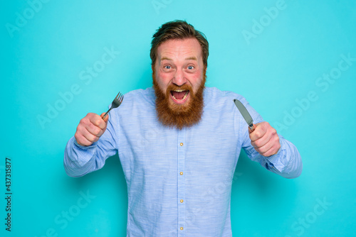 Hungry man with tattoos is ready to eat with cutlery in hand photo