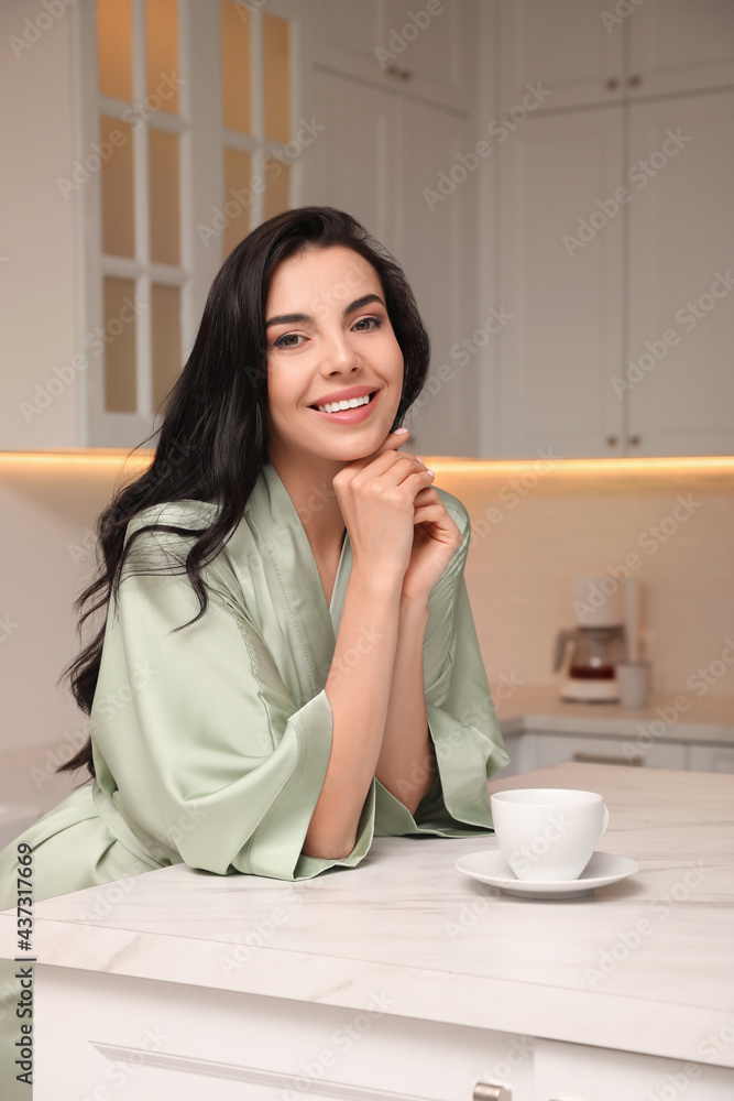 Pretty young woman wearing beautiful silk robe with cup of coffee in kitchen Pretty young woman wearing beautiful silk robe with cup of coffee in kitchen