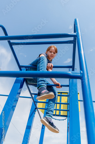 Young girl climbs the bar on the playground. Child sports concept. Healthy lifestyle.
