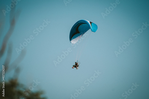 Blue and white motorized parachute flying over a blue sky photo