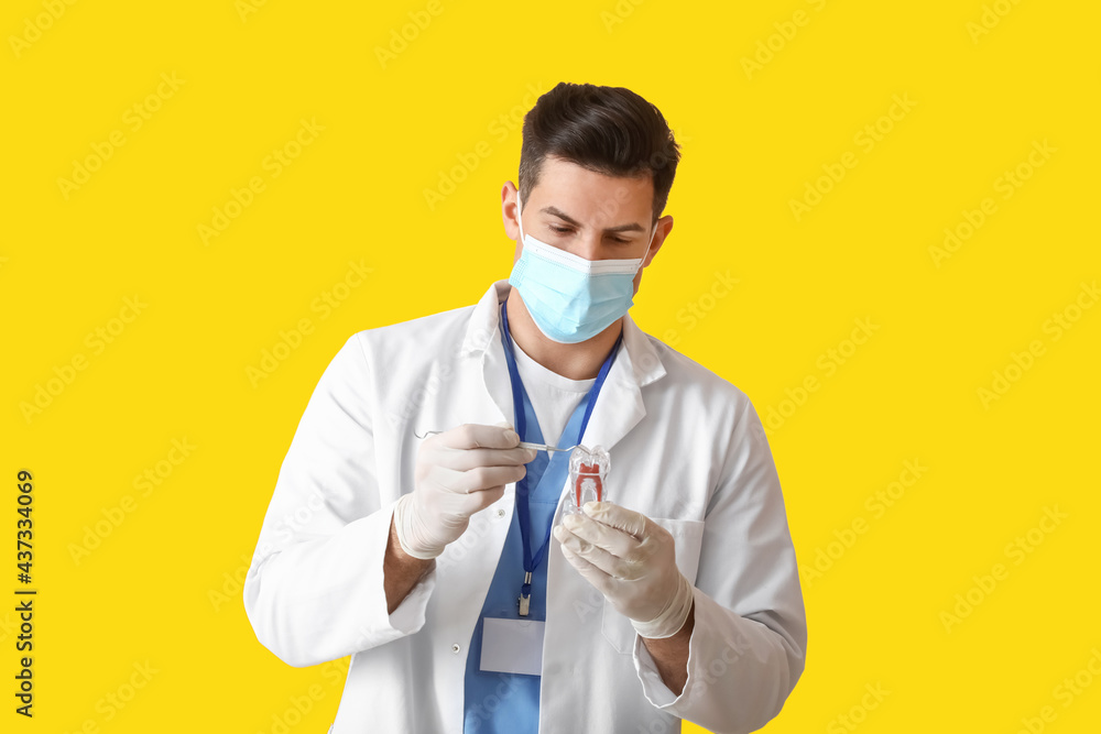 Male dentist in mask with plastic tooth on color background Male dentist in mask with plastic tooth on color background