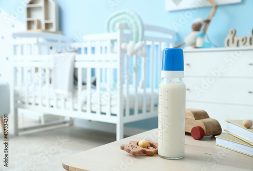 Bottle of milk for baby and toys on table in room photo