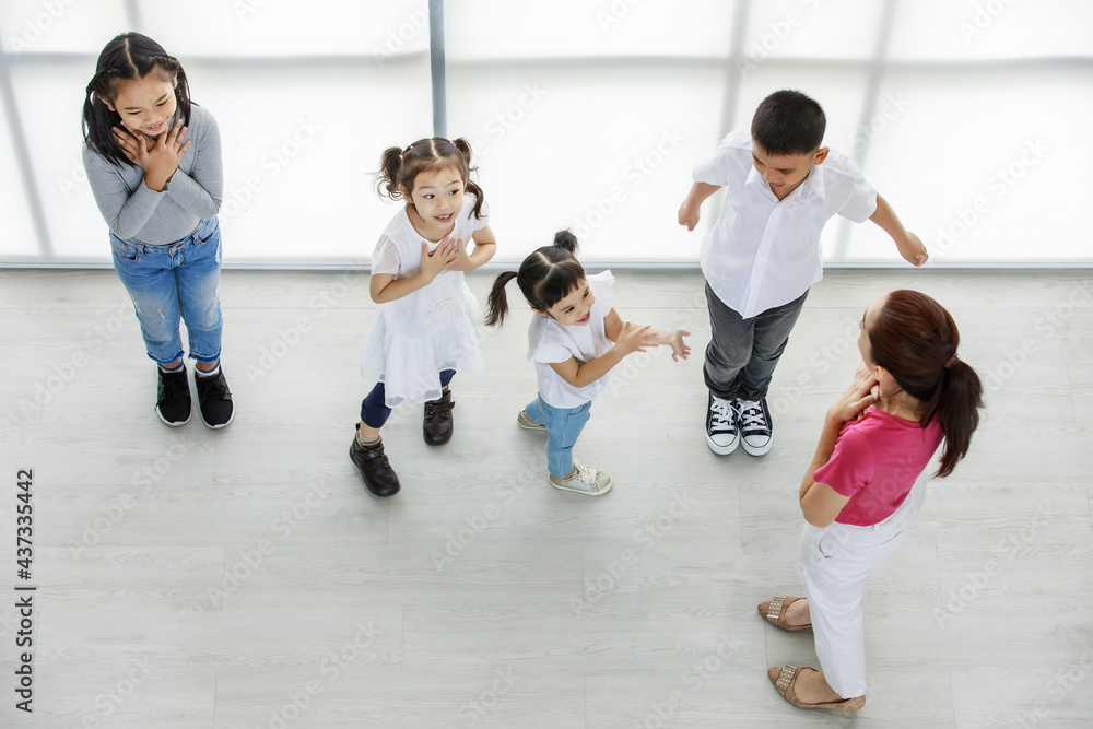 Fototapeta premium Top view shot of Asian female primary education school perfomance teacher teaching group of little boy and girls to perform happy fun private kindergarten acting class