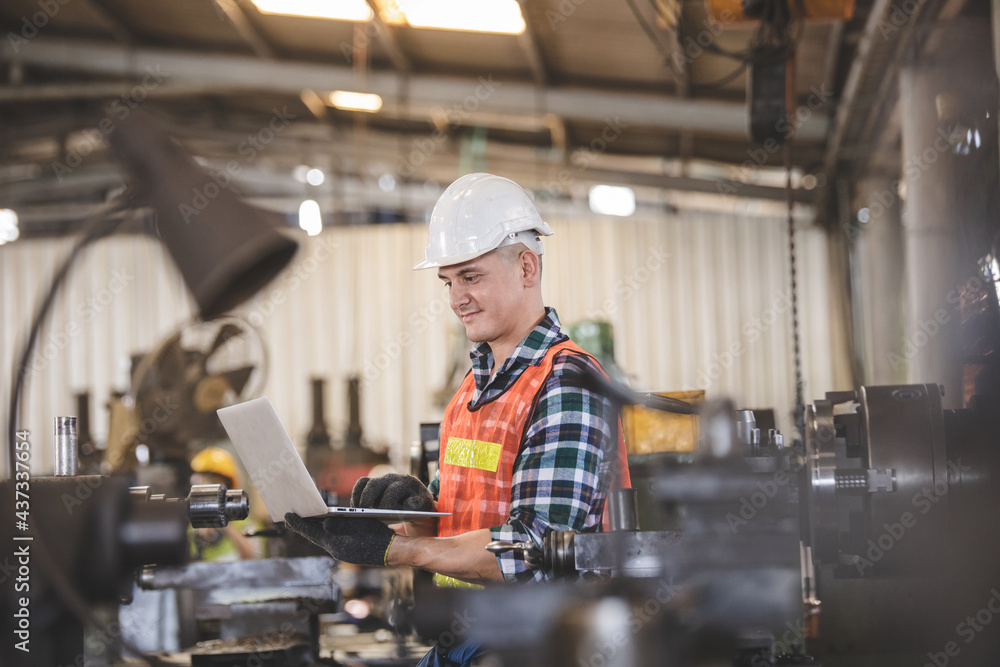 man Lathe worker in production plant drilling at machine on the factory. Industrial engineer worker holding laptop Inspect workpieces