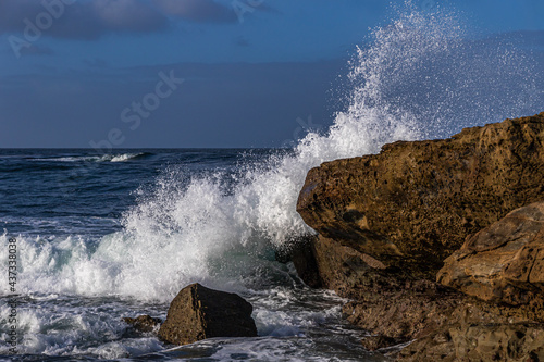 Wave breaking on rock in Laguna Beach, California. Spray in the air. Pacific ocean, blue sky and clouds in background. 